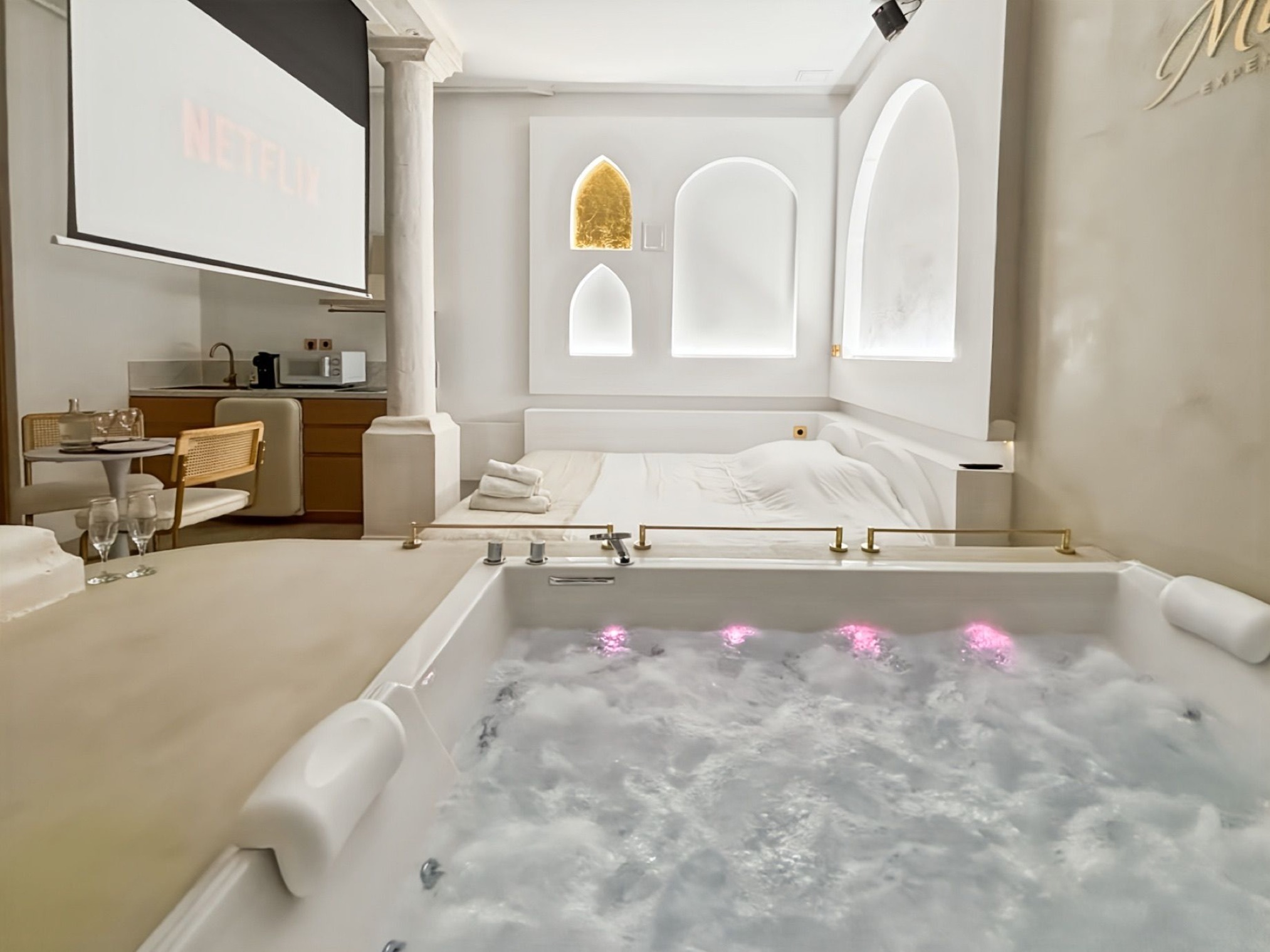 Wide view of the Balnéo Room with lit jacuzzi, screen and dining corner